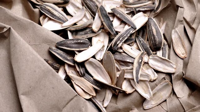 A hand throwing the husks of shelled sunflower seeds onto crumpled used paper