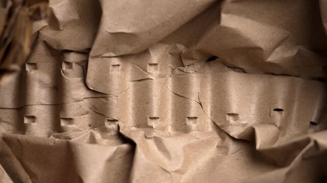 Hands compressing and releasing crumpled kraft paper demonstrating flexibility with softness. Brown packing material changing shape under pressure. Protective wrapping concept