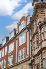 Obraz premium Classic British architecture lines a traditional London street, with red brick buildings and historic facades beneath a cloudy sky.