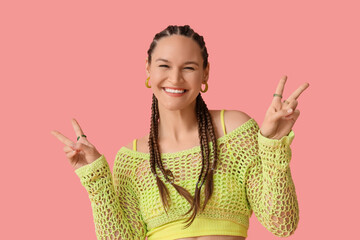Young woman in crochet top with dreadlocks showing victory gesture on pink background