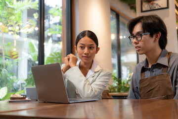 Focused business consultant showing sales performance or marketing strategy to a cafe owner on a laptop screen in a modern coffee shop.