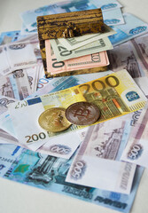 Obraz premium Two Bitcoin coins, a chest of dollars, and a Euro banknote against a background of Russian rubles. Concept of the transition to cashless payments and digital money. Trading. Cryptocurrency mining.