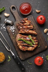 Cut grilled steak with tomatoes, ketchup and fork on black grunge background