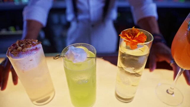 Bartender presenting a row of colorful cocktails on an illuminated bar counter