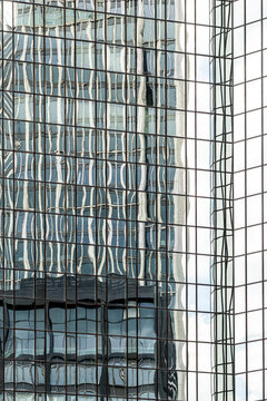 Modern skyscraper glass facade shows abstract reflection with gentle distortion creating a vertical architecture pattern that feels fluid and graphic