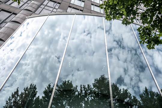 Modern urban architecture in daylight with glass facade reflection of sky clouds and trees creating a serene pattern on windows