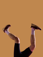 Male legs in brown sneakers and white socks bent on beige background. Concept of mens footwear promotion, everyday outfit campaign, ecommerce product display and retail advertising use.