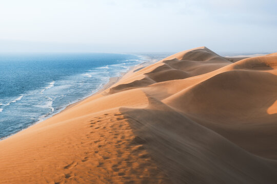 View of sun-kissed dunes meet the azure sea, creating a breathtaking contrast of warm sands and cool waters along the coast, Walvis Bay, Erongo Region, Namibia.