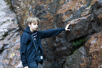 Obraz premium Boy touching wet rock at Cossack waterfall in Teberda Nature Reserve
