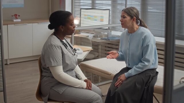 Professional healthcare consultation with African American female doctor and Caucasian female patient talking in modern clinic office during medical appointment