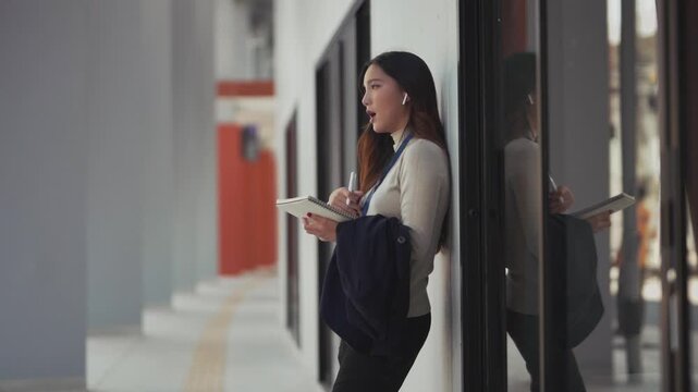 Asian business woman stays productive with earbuds during work call outdoors