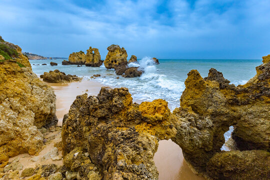 View of golden cliffs embrace the turquoise sea as waves crash against the rugged rocks, creating a dynamic coastal scene, Oeiras, Lisboa, Portugal.