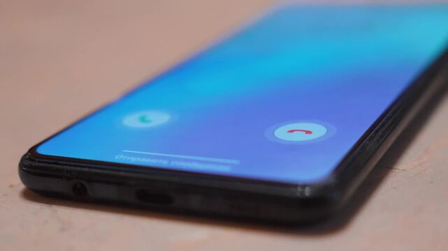 Detailed macro shot of a modern smartphone lying on a table receiving an incoming phone call, with green and red buttons to accept or decline the communication request on its vibrant screen
