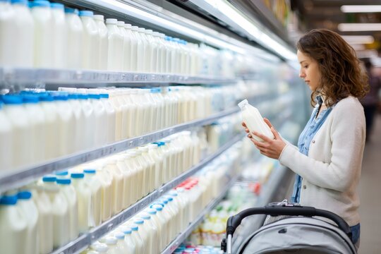 A young woman shops for milk in the dairy aisle of a grocery store. Female customer choosing a fresh product from the refrigerator shelf. Healthy eating and consumer choice concept