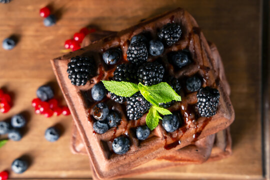 Sweet chocolate Belgian waffles with fresh blackberries, blueberries and mint on wooden background