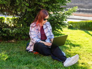 Woman using laptop outdoor under tree. Freelancer working on computer. Remote work and digital nomad lifestyle concept