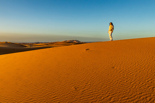 A person stands atop a large sand dune under a clear blue sky. Mezouga,Sahara desert,Morocco