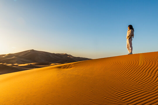 A person stands atop a large sand dune, gazing at the horizon under a clear blue sky. Mezouga,Sahara desert,Morocco