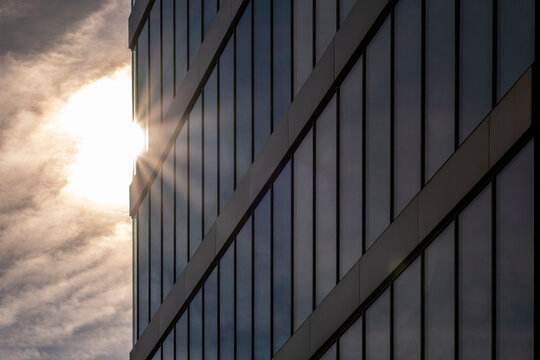Sunlight hits modern glass office building facade as clouded sky adds contrast creating dramatic architecture detail for contemporary business background