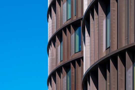 Modern curved glass tower building facade with blue sky showcases pattern and clean architecture lines for minimal contemporary exterior background