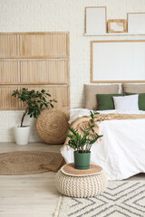 Soft bed, pouf, houseplants and picture in stylish bedroom