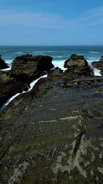 Vertical drone footage showing dramatic cliff edges and deep blue ocean horizon at Karang Taraje Beach, Sawarna, Banten. Natural rock formations and rolling waves create a powerful coastal landscape.