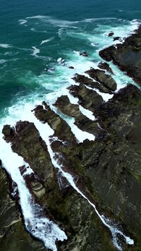 Drone aerial view capturing abstract parallel rock lines with waves breaking between them at Sawarna Beach, Banten, Indonesia. Strong natural geometry and ocean textures framed in Vertical format.