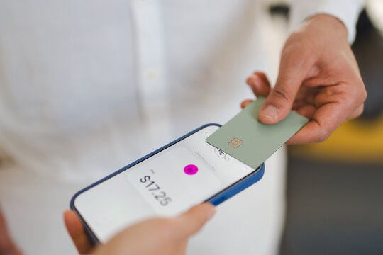 A person holds a credit card near a smartphone screen displaying a payment amount of $17.25, indicating a contactless transaction.