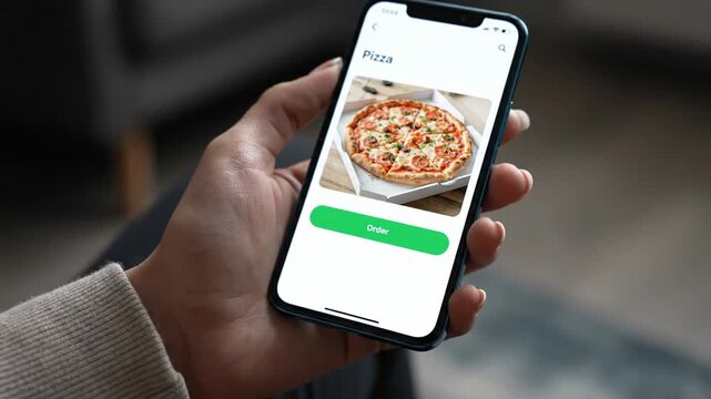 Person holding a smartphone displaying a delicious pizza image on its screen with an "Order" button. Ordering food online.