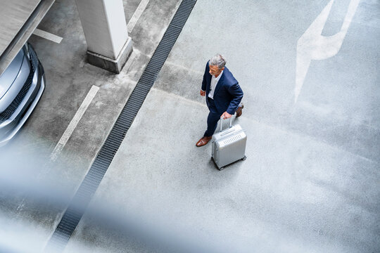 Businessman walking with wheeled luggage in parking lot