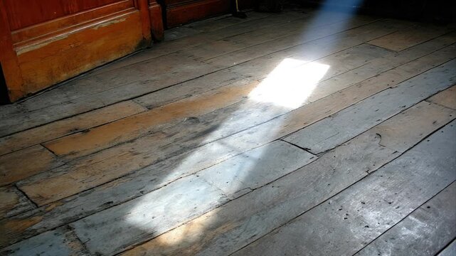 Angled shot of aged, wooden floorboards with a beam of sunlight. A door frame is on the left