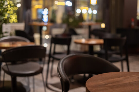 blurred cozy cafe interior at night with warm bokeh lights, wooden tables and elegant dark chairs, perfect background for restaurant or bistro themes