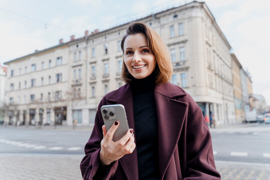 Smiling woman with smartphone outdoors in urban city setting