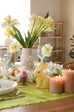 Festive table setting decorated with spring flowers, candles and Easter bunnies in kitchen