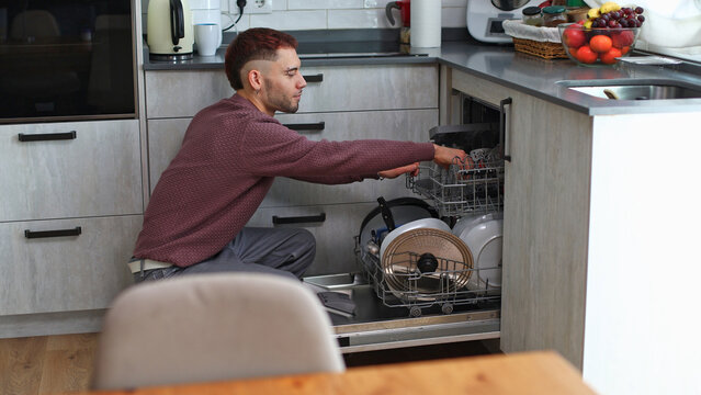 Young man loading dishwasher in modern kitchen
