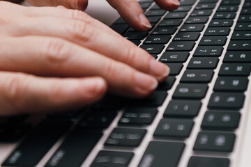 Close-up of female hands typing on a modern laptop keyboard in a home office.