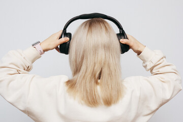 Blonde woman holding black wireless headphones while sitting at a laptop.