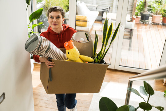 Person carrying a box with home items while moving indoors smiling