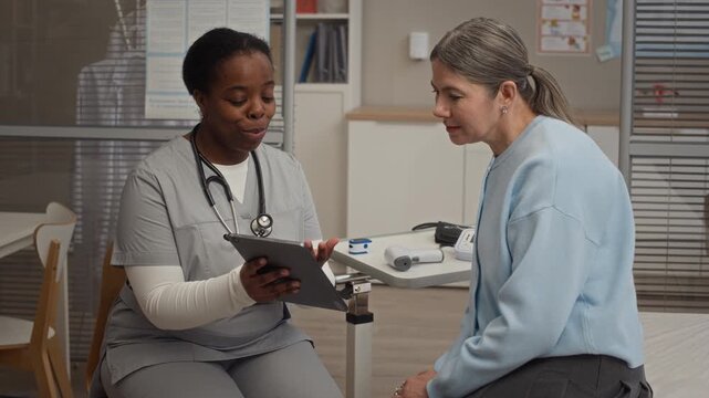 Black female healthcare professional reviewing medical test results on tablet with Caucasian female patient during consultation in modern clinic office