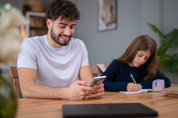 Fototapeta premium Father distracted by phone while daughter doing homework