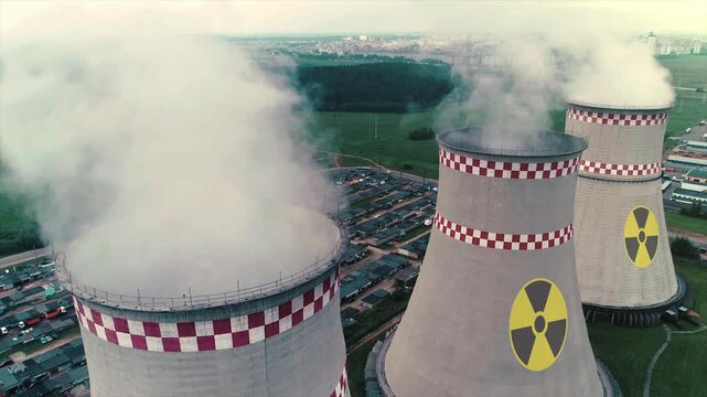 Aerial drone view of nuclear power plant cooling towers emitting steam into the sky. Industrial energy facility with radioactive hazard symbols on large concrete reactors. Electricity generation, 4k.