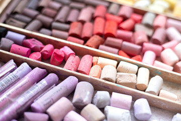 Soft pastel chalk set in pink, red, yellow, and brown in a wooden art supply case. Multicolored artist's background