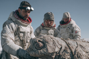Three astronauts examine a large, strange creature.