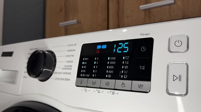 Selecting wash cycle on modern washing machine control panel. Close up of hand choosing specific laundry program for fabric care. Digital display with eco, cotton and delicate wash options.