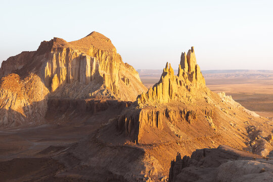 View of sun-kissed, rugged rock formations rise majestically from the arid landscape, casting long shadows in this striking desert scene, Shetpe, Mangystau Region, Kazakhstan.