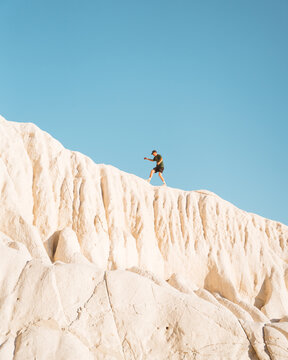 View of a lone figure standing atop the weathered, pale cliffs under a bright azure sky, a striking contrast of textures and colors, Aktau, Mangystau Region, Kazakhstan.