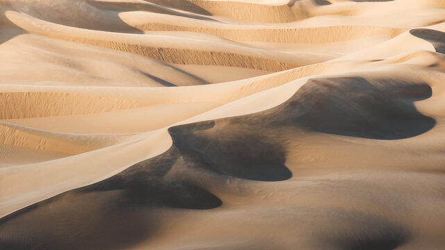 View of sun-kissed dunes rippling across the vast expanse, casting long shadows and creating a mesmerizing dance of light and shadow, Senek, Mangystau Region, Kazakhstan.