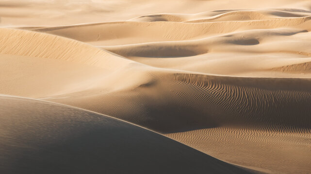 View of undulating sand dunes bask in the warm glow of the sun, creating a mesmerizing pattern of light and shadow, Senek, Mangystau Region, Kazakhstan.