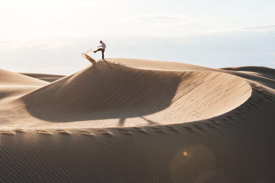 View of a lone figure atop a sand dune, poised to destroy a laptop in the vast desert landscape, bathed in the warm glow, Senek, Mangystau Region, Kazakhstan.