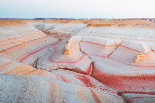 View of layered sandstone formations with a striking palette of white, orange, and red hues carved by erosion under a clear sky, Kyzylkup, Mangystau Region, Kazakhstan.
